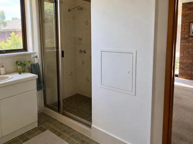 Bathroom wall with small access panel beside shower and vanity in a tiled home interior in Baulkham Hills